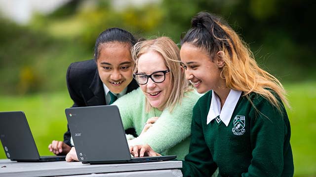 two students and a teacher looking at a laptop