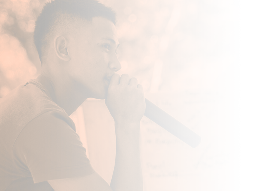 A photograph of a Māori boy holding a microphone to his mouth with a handwritten presentation behind him. 