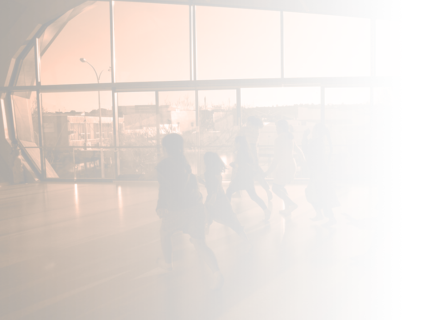 A photograph of a group of children running away from the camera into a sunlit dance studio. 