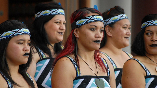 A chest-up photograph of five Māori women in kapa haka performance attire. 