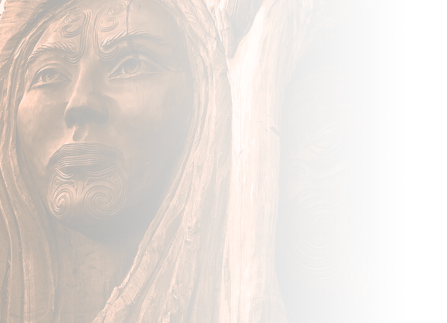 A photograph of driftwood carvings, showing two faces with facial tāmoko, a woman on the left and a man on the right. 