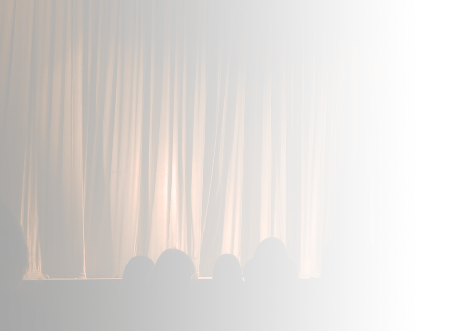 A photograph of the silhouette of an audience waiting in front of a stage obscured by red curtains. 