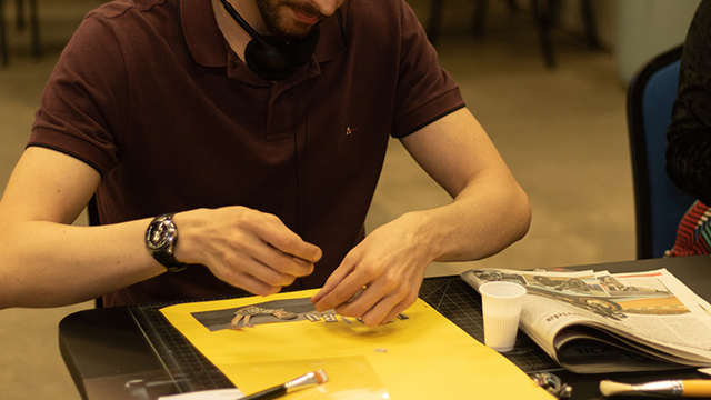 A photograph of a person with their face obscured making a collage using newspaper and art supplies. 