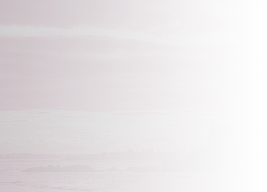 A beach at sunset. Boulders near the shore are silhouetted against a bright, cloudy sky