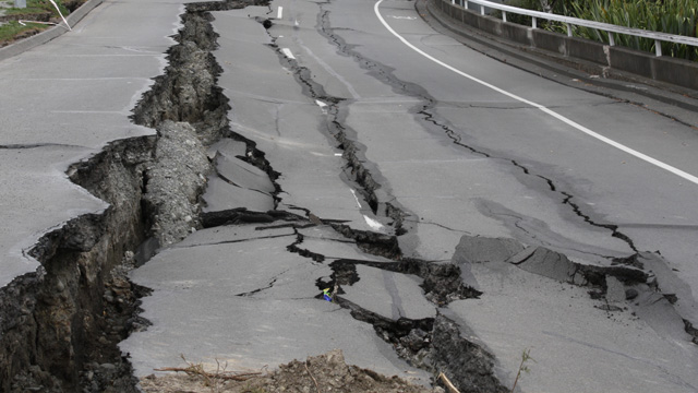 A road has been badly damaged by an earthquake. The surface is deeply cracked, and the road falls away to the right.