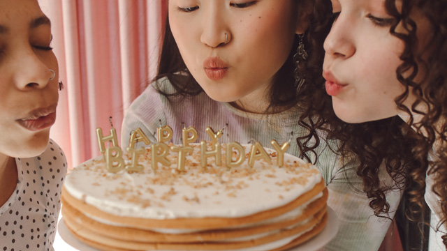Three young people blowing out the candles on a birthday cake