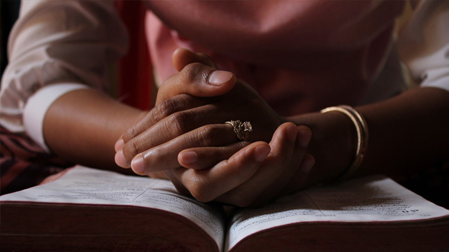 Clasped hands resting on an open book