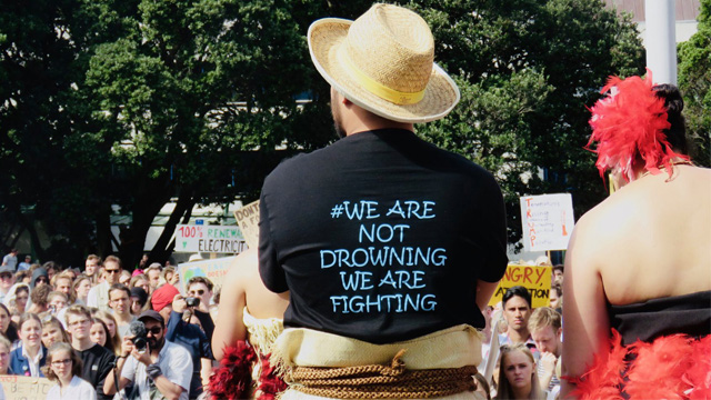 Someone stands facing the 2019 Climate Strike. The text on their shirt reads "#We are not drowning, we are fighting"