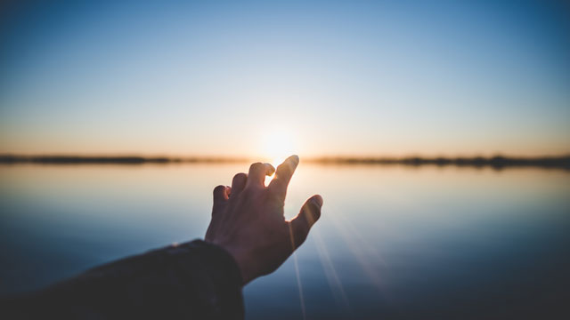 hand reaching out to sunrise