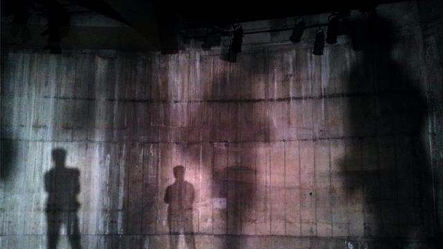 Tall shadows of people cast on the wall of an industrial theatre space