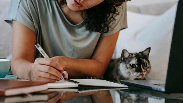 young woman writing in notebook and sitting next to a cat