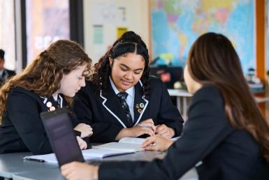 Three students studying together at a table in a classroom